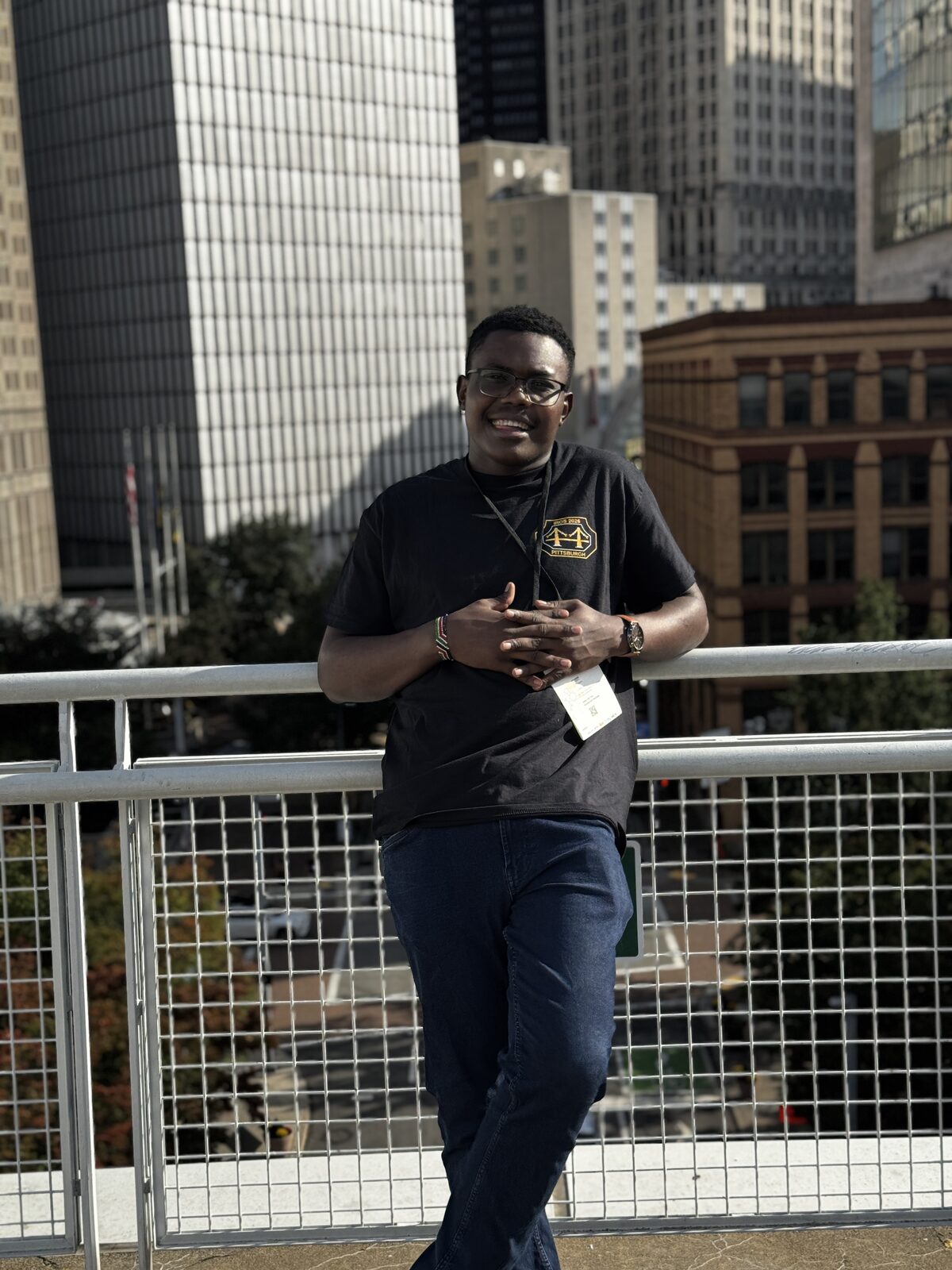 Austine leaning on a railing in an IROS 2026 shirt with downtown Pittsburgh buildings behind